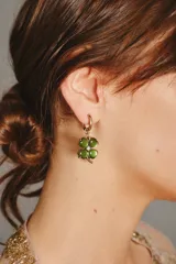 Aro tipo argolla dorada con dije colgante de trébol de cuatro hojas en color verde, con un pequeño cristal en el centro.