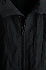 Campera rompevientos de nylon color negro, repelente al agua, con cuello elevado, cierre frontal y bolsillos laterales. Cuenta con forro de malla y puños con elástico.