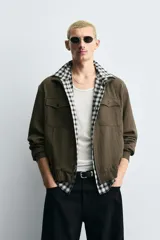 Cazadora de hombre color verde oliva, estilo bomber o Harrington, con cuello subido, cierre frontal de cremallera y puños y bajo elásticos. Presenta bolsillos de plastrón con solapa en el pecho y bolsillos de vivo en la cadera.