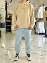 Canguro oversize color beige, con capucha y amplio estampado tipográfico en la espalda.