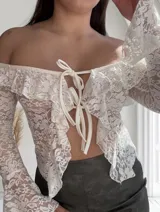 Top de encaje blanco con mangas largas acampanadas, hombros descubiertos, volados y lazo ajustable en el frente.