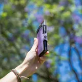 Billetera tarjetero automática con estructura de aluminio y revestimiento de cuero bicolor en tonos verde oliva y beige. Cuenta con un cierre de broche a presión y el logo de la marca grabado en la parte inferior.