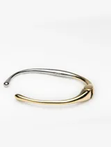Pulsera rígida de diseño minimalista con acabado bicolor en tonos dorado y plateado. Presenta una estructura metálica con apertura de bisagra y extremos abiertos redondeados.