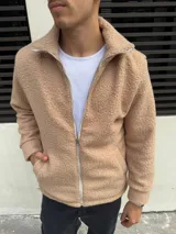 Campera de corderito color beige con cierre frontal completo y cuello alto. Presenta puños y ruedo acanalados, con detalles de terminación en tela lisa a lo largo del cierre.