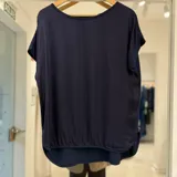 Blusa de manga corta color azul marino, de corte holgado, con cuello redondo y diseño de doble capa en el bajo con dobladillo curvo.