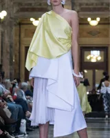 Falda asimétrica de tiro alto color blanco, confeccionada en seda triple. En la delantera posee tres tablones escalonados y una pieza en gasa translúcida plisada, que poco a poco van definiendo el largo irregular del diseño.