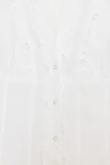 Camisa de popelín con cuello redondo y escote en pico, manga corta abullonada con elástico y cierre frontal con botones. Presenta detalles de volantes a lo largo de la abertura frontal.