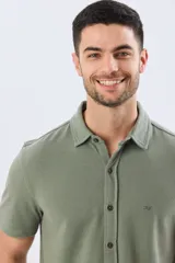 Camisa de piqué lisa color celeste, de manga corta, con cuello camisero y cierre frontal de botones oscuros.