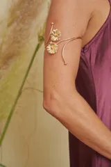 Brazalete dorado con diseño de dos flores y detalles de esferas en los extremos.