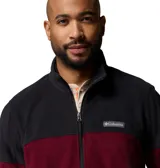 Campera polar Columbia con cierre frontal completo y cuello alto. Presenta un diseño de bloques de color con la parte superior en negro y la inferior en bordó, incluyendo bolsillos laterales con cierre y logo de la marca en el pecho.