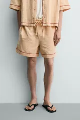 Shorts relaxed fit color beige con textura en relieve tipo jacquard, cintura elástica con cordón ajustable y detalle de bordado en contraste en el bajo.