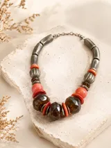Collar de diseño artesanal compuesto por una combinación de cuentas de resina en tonos ámbar, coral y naranja, intercaladas con piezas metálicas cilíndricas y esféricas estriadas.