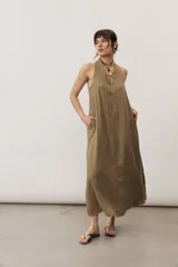 Vestido largo color marrón, sin mangas y con escote halter. Cuenta con bolsillos laterales y corte holgado.