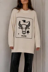Sweater de punto negro con diseño oversize, cuello redondo y manga larga. Presenta un bordado frontal en color crudo con motivo del signo del zodíaco Géminis, acompañado de detalles de sol, luna y estrellas dentro de un recuadro.