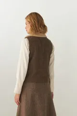 Chaleco corto de corte recto, confeccionado en lana fina sin teñir, con cuello de piel sintética y bolsillos frontales con detalles en cuero.