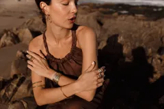 Blusa color salmón/rosado claro, confeccionada en lino, con escote recogido y tiras trenzadas regulables que cruzan en la espalda. Presenta un elástico fruncido en la cintura que da lugar a un pequeño volante con terminación deshilachada.