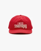 Gorra de béisbol de cinco paneles sin estructura color rojo, con visera plana y bordado frontal en tono crudo con la frase 'I NEED Therapy'. Presenta detalles bordados adicionales y correa ajustable de nailon en la parte trasera.