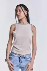 Musculosa color crudo de tejido estriado, con cuello redondo y sisas decoradas con tachas metálicas plateadas.