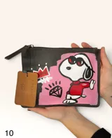 Sobre de cuero marrón con diseño pintado a mano que presenta al personaje Snoopy sobre un fondo rosado y la palabra 'heal'. Cuenta con cierre superior y etiqueta de cuero colgante.