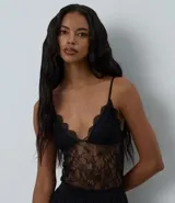 Body de encaje negro con transparencias, escote en V profundo y breteles finos ajustables. Cuenta con copas integradas y cierre inferior.