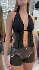 Top negro de tirantes con escote halter, confeccionado en tela transparente con bordados de lentejuelas y diseño abierto en el frente.