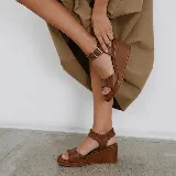 Sandalias de plataforma tipo cuña, color marrón, con tiras de cuero texturizado y costuras decorativas. Cuentan con tira al tobillo con hebilla metálica y plataforma corrida.