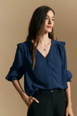 Camisa de manga larga color azul marino, con escote en V y cierre frontal de botones. Presenta detalles de volados en los hombros, frunces en la espalda y puños elastizados con terminación de volado.