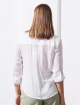 Blusa blanca de gasa marca Zac & Rachel, con cuello a la base, escote en V, abertura central con botones, bolsillo aplicado en el pecho y mangas largas regulables con presilla y botón. Tiene terminación opcional de nudo en el ruedo.