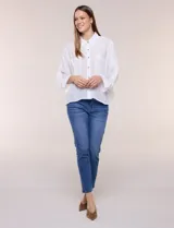 Camisa blanca de silueta holgada y textura liviana, con cuello camisero clásico, abotonadura frontal con botones en contraste y doble bolsillo de parche en el frente. Cuenta con mangas de corte dolman de largo tres cuartos con puño amplio y ruedo recto con aberturas laterales.