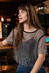 Top de red con brillo metalizado, de corte recto y manga corta. Presenta un diseño translúcido con acabado brillante, ideal para superponer sobre otras prendas.