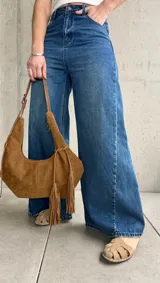 Jean wide leg de tiro medio-alto, color azul con lavado clásico y efecto desgastado. Presenta costuras laterales destacadas que estilizan la silueta, bolsillos delanteros y traseros, y cierre frontal con botón metálico y cremallera.
