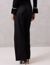 Pantalón palazzo de satén color negro, de tiro alto con pretina delantera estructurada, pasadores para cinturón y bolsillos laterales. Presenta una caída fluida y amplia, con elástico en la parte posterior de la cintura para mayor ajuste.