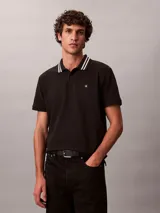 Chomba de piqué Calvin Klein color negro, con cuello clásico y ribetes a rayas blancas, cartera de dos botones y pequeño monograma CK bordado en el pecho.