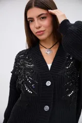 Saco de punto grueso color negro, con escote en V, cierre frontal de botones y mangas largas. Presenta detalles de bordado con lentejuelas y canutillos negros y plateados en la parte superior delantera.