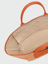 Bolso tipo tote de gran tamaño confeccionado en tejido de paja con rayas multicolores. Presenta un parche frontal de cuero naranja con el logo de la marca grabado, asas de hombro de cuero a juego y un detalle colgante de cuentas de madera. Incluye un cierre de mosquetón metálico en la base.