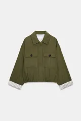 Chaqueta corta de color verde militar, con cuello solapa, bolsillos delanteros con solapa y cierre frontal de botones ocultos. Presenta mangas amplias con vuelta en los puños que muestran un forro a rayas.