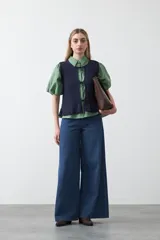 Chaleco tejido color verde musgo, con trama texturada, cuello a la base y cierre frontal con lazos. Presenta un ruedo con volado.