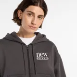 Campera con cierre frontal completo y capucha, confeccionada en tejido polar color gris oscuro. Presenta un diseño de corte holgado con bolsillos frontales tipo canguro y el logo de la marca estampado en el pecho.