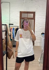 Remera blanca de corte holgado con cuello redondo y manga corta. Presenta un pequeño estampado frontal con texto en rosado y un limón cortado.