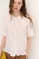 Camisa de manga corta color blanco con cuello mao y cierre frontal de botones. Presenta detalles bordados tono sobre tono en el canesú y diseño de corte recto.