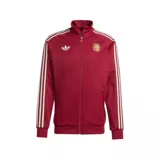 Campera deportiva Adidas de la selección de España, color bordó con cierre frontal, cuello alto y las icónicas tres tiras blancas en las mangas. Presenta el logo de Adidas Originals en el pecho derecho y el escudo de la selección en el pecho izquierdo.