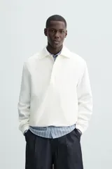 Cazadora tipo canguro de calce relajado, color blanco roto o crema, confeccionada en mezcla de lyocell y algodón. Presenta cuello solapa con cierre frontal de botonadura oculta, manga larga con puños elásticos y bolsillos frontales de vivo. El bajo es ajustable con elástico oculto en los laterales.