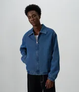 Campera estilo bomber de jean color azul, con cierre frontal, cuello camisero, puños y ruedo con elástico, de corte boxy amplio y estructurado.