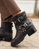 Botas de cuero estilo biker en color marrón oscuro con efecto desgastado. Presentan un diseño de caña corta con correas ajustables con hebillas metálicas y detalles de remaches. Cuentan con una suela de goma dentada y tacón bajo.