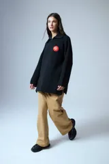 Sweater negro de cuello polo tejido con cierre diente de perro a tono y tajos laterales. Tiene un parche bordado con elementos del drop.