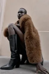 Bota alta de cuero negro, estilo cowboy, con tacón de bloque alto y punta cuadrada. Presenta costuras decorativas en el cuerpo de la caña.