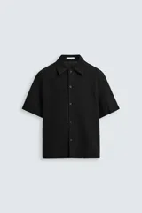Camisa negra de manga corta con cuello solapa y cierre frontal de botonadura. Presenta un tejido con estructura abierta y patrón jacquard geométrico.