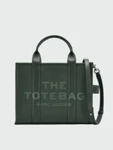 Bolso tipo tote de cuero negro, modelo The Leather Medium Tote Bag de Marc Jacobs. Presenta doble asa superior, correa ajustable para el hombro y el texto grabado "THE TOTE BAG MARC JACOBS" en el frente.