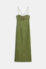 Vestido midi verde militar con estampado de lunares rosados, de corte recto y tirantes finos cruzados en la espalda. Presenta escote con frunces y detalle de lazo en el centro.