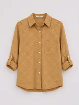 Camisa de manga larga con cuello camisero, confeccionada en algodón con textura geométrica en relieve. Presenta cierre frontal con botones, un bolsillo en el pecho y mangas con sistema de ajuste mediante botón.
